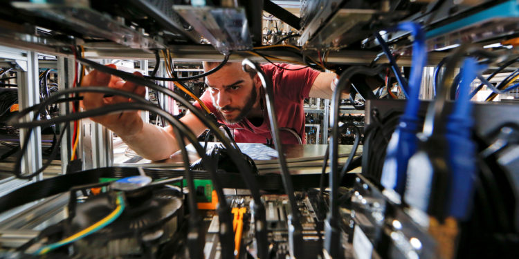 An employee works on bitcoin mining computers at Bitminer factory in Florence | 動區動趨-最具影響力的區塊鏈新聞媒體 回顧|比特幣耗能議題似曾相識?網路在 1999 年也被批評浪費電