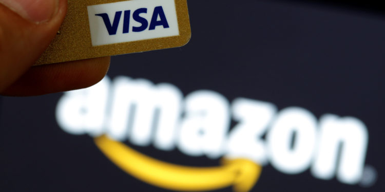 A visa credit card is held in front of an Amazon logo in this picture illustration | 動區動趨-最具影響力的區塊鏈新聞媒體 亞馬遜宣布:拒絕英國發行的 Visa 信用卡,手續費過高!Visa股價跌5%